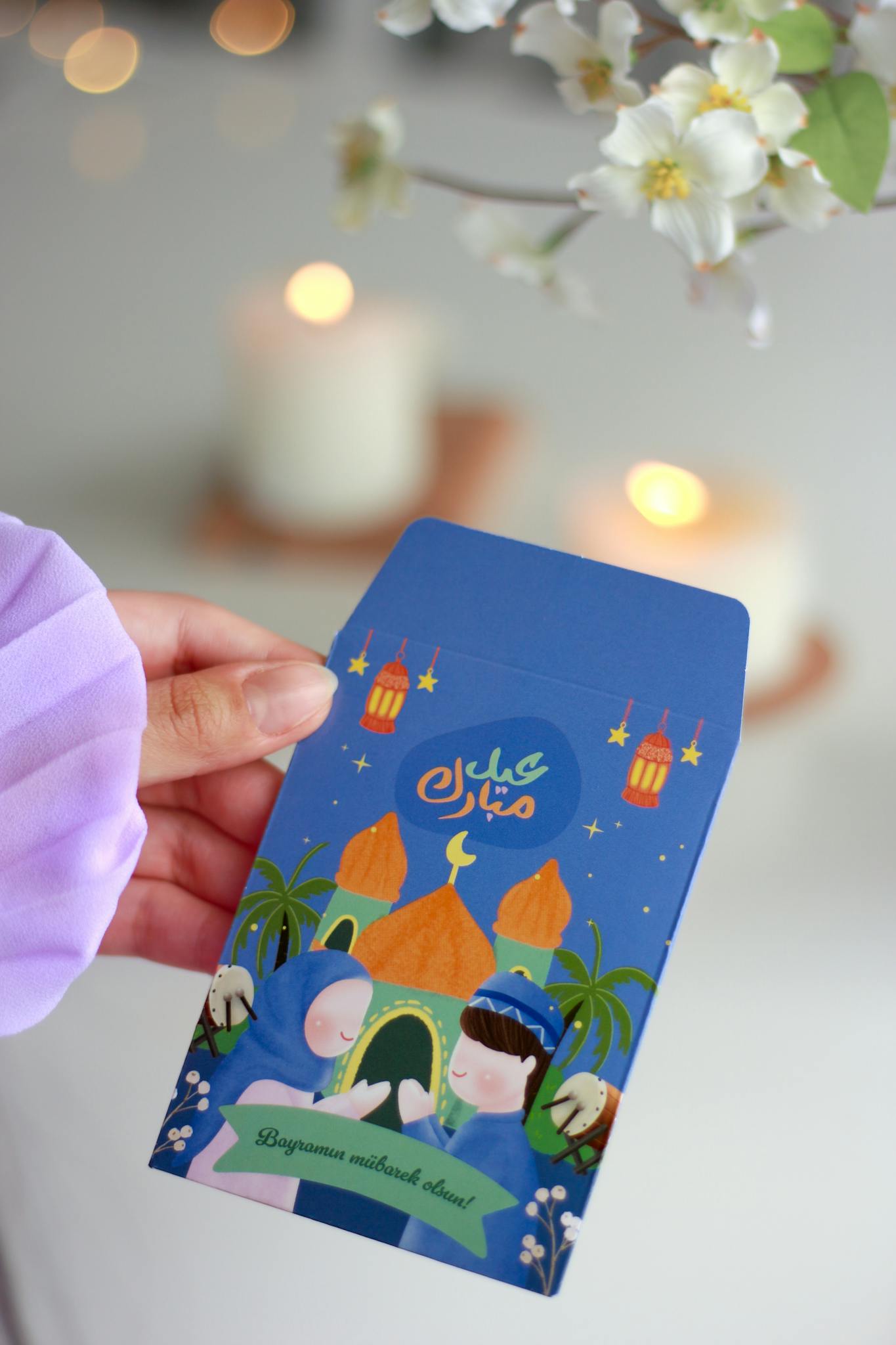 A vibrant Eid Mubarak card featuring mosque and children illustration, held by a hand.